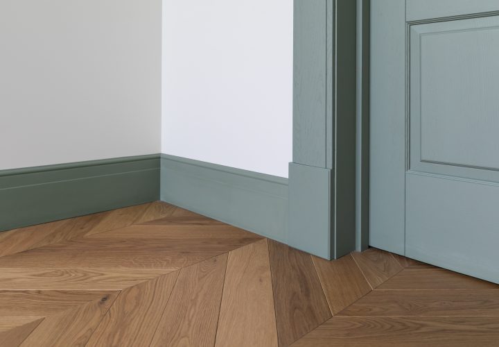 Fragment of classic interior with french herringbone parquet floor and green door and skirting boards. The final stage of finishing works in the apartment