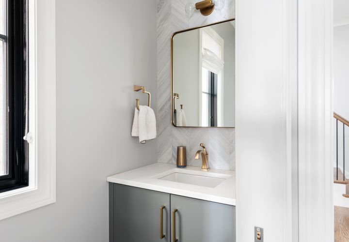 Contemporary White and Gray Half Bathroom. Gray bathroom vanity with gold fixtures and mirror showing into hallway.